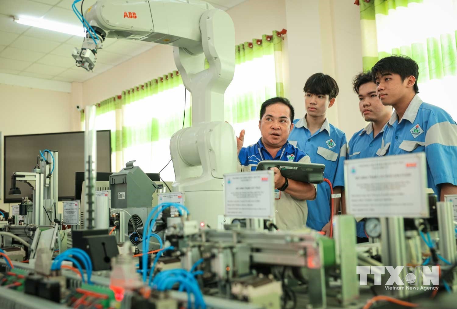 Thạc sĩ Hồ Tấn Đạt – Giảng viên khoa Điện tử hướng dẫn sinh viên điều khiển, làm chủ vận hành cánh tay robot. (Ảnh: Hoàng Hiếu/TTXVN)